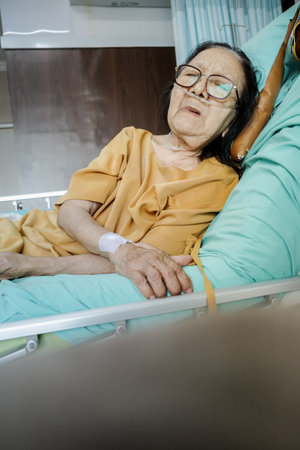 Sick Southeast Asian female senior patient with respiratory disorder having bedrest in hospital