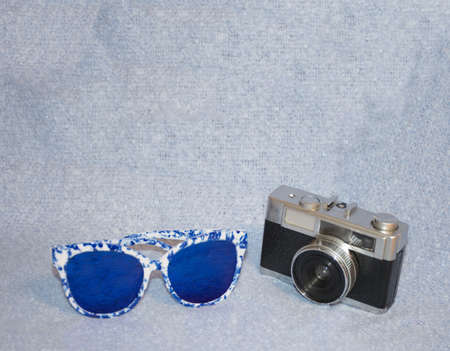 Bluish vibrations that evoke memories of summer pleasures. Vintage camera with glasses on bluish material. Minimalist conceptの写真素材