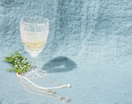 Glass of champagne with golden and pearls necklace, and pine leaves on bluish background. Minimalist conceptの写真素材