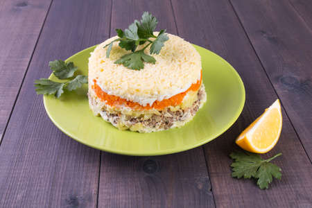 Festive layered round salad with vegetables and salmon fish Mimosa on a plate on a wooden backgroundの写真素材