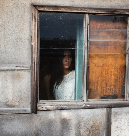 girl by the window in a wooden old abandoned house with dim lightの写真素材