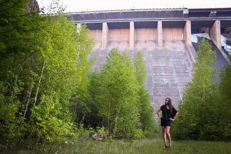 A dreamy young brunette girl stay near hydroelectric power station. Evening time. Side view.の写真素材