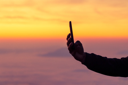 Silhouette of man hand taking a photo on sunrise with mobile phoneの写真素材