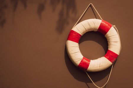 red and white safety torus or lifebuoy hanging on brown wall background