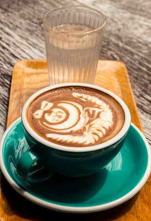 Hot mocha coffee with latte art and glass of water on wooden tableの写真素材