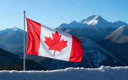 Canadian flag waving in the wind over snowy mountains and blue sky.の素材