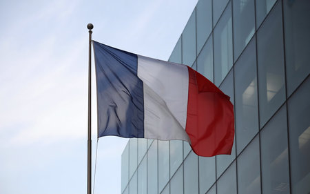Flag of France waving in the wind in front of a glass buildingの素材