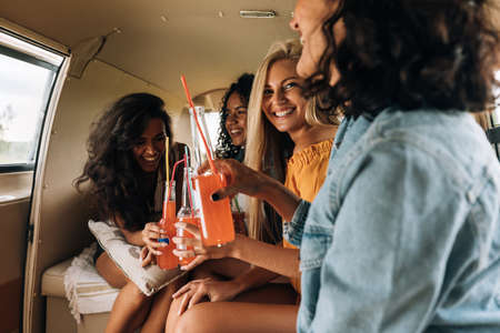 Four women drinking cocktails in camper van enjoying summer