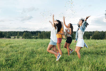 Side view of four female friends running on a field and throwing confettiの写真素材