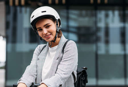 Beautiful smiling businesswoman in cycling helmet lean on handlebar of electric scooter looking at cameraの写真素材