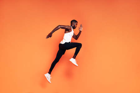 Male runner doing fitness workout. Athlete exercising over an orange background.の写真素材