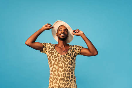 Smiling stylish man holding his straw hat and looking up against the blue backgroundの写真素材