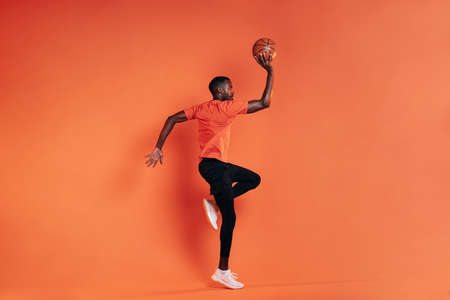 Side view of sportsman jumping in the air with basket ball in hand. Male in sportswear exercising...