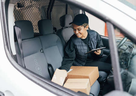 Smiling woman sitting on driver's seat checking packages and holding a digital tabletの写真素材