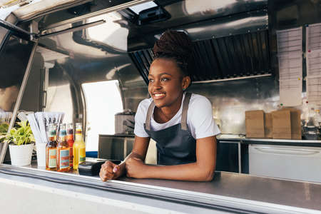 Smiling saleswoman in apron leaning counter standing in a food truckの写真素材