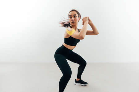 Woman with kinesiology tape on her shoulder exercising indoors. Young female doing sit ups.