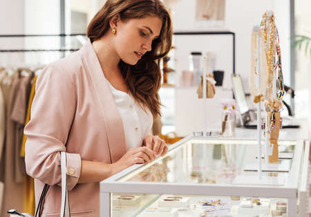 Female buyer looking at display case in a boutique. Woman in boutique choosing accessories.の写真素材