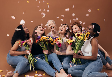 Group of diverse women with bouquets having fun under falling petals. Six happy females sitting together against a brown background.の写真素材