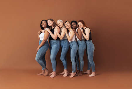 Full length of six smiling women embracing in studio. Females of different ages and body types posing over brown background.の写真素材