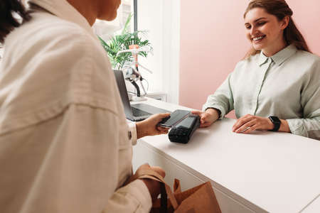 Female customer paying through phone at store. Small boutique owner receiving payment from buyer.