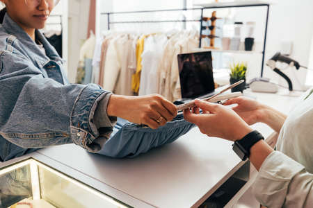 Female buyer giving clothes to unrecognizable clerk for checkout