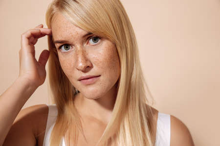 Close up portrait of a young beautiful woman with freckles posing in studio over pastel backgroundの写真素材