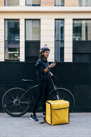 Woman courier in uniform standing in the city holding smartphone checking customer addressの写真素材