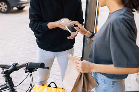 Woman receiving food delivery at the doorway. Midsection of an unrecognizable woman making a sign on a smartphone.の写真素材