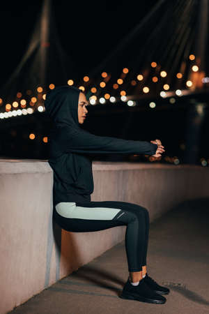 Side view of a young fit woman doing wall squat. Sportswoman doing wall sit at night.の写真素材