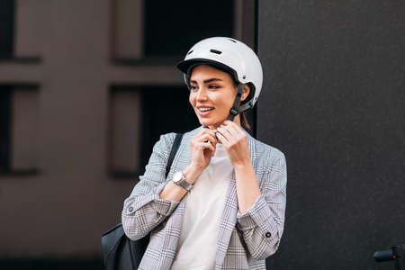 Young smiling woman fasten safety helmet on her head. Businesswoman preparing for a ride on electrical scooter.の写真素材