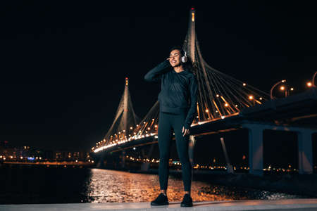 Full length of sportswoman standing outdoors at night listening to music during fitness trainingの写真素材