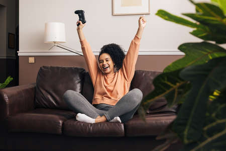 Happy mixed race woman sitting on a sofa in living room with raise hands upの写真素材