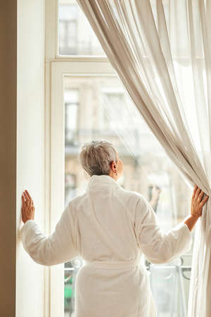 Mature woman relaxing on a bed. Senior female in bathrobe making an online payment at home.の写真素材