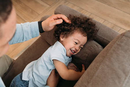 Father and his young son playing on the sofa. Happy little boy laughing while lying on a couch.の写真素材