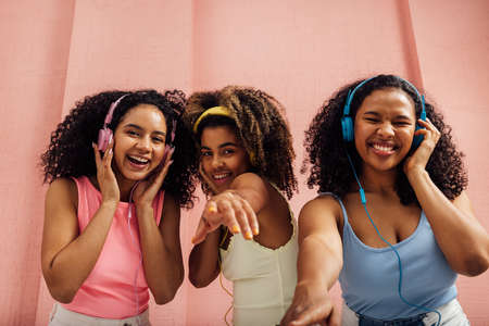 Three laughing women with curly hair dancing together and looking at camera, wearing headphonesの写真素材