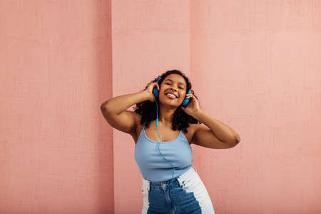 Plus size female wearing blue headphones and dancing against pink wallの写真素材