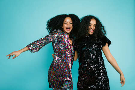 Two happy girlfriends raised hands up, standing in studio at blue wallの写真素材