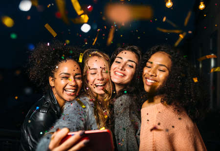 Outdoor shot of group friends laughing under confetti