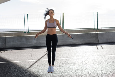 Young fit woman exercising with skipping rope outdoors