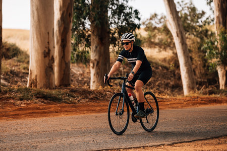 Professional cyclist in sportswear riding her bike on countryside roadの写真素材
