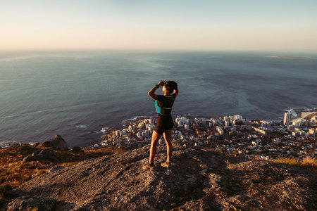 Woman hiker enjoying the view at sunset. Trail runner taking a break standing on the top of the...