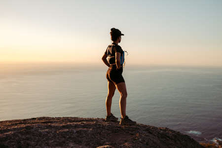 Woman hiker enjoying the view at sunset. Trail runner taking a break standing on the top of the mountain.の写真素材