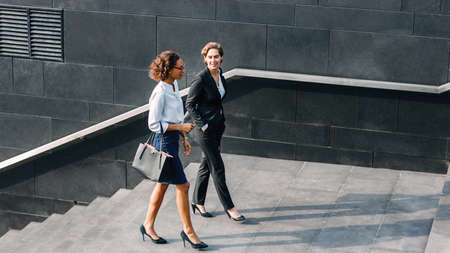Young businesswoman discussing with her colleague while walking down the stairs near an office buildingの写真素材