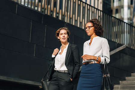 Young businesswoman discussing with her colleague while walking down the stairs near an office buildingの写真素材