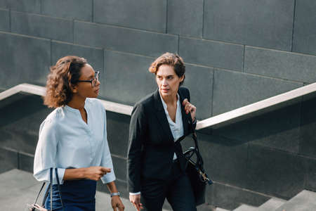 Two women commuting to the office in the day carrying office bags. Ceo and her assistant walking on a city street.の写真素材