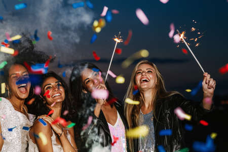 Happy friends with sparklers at sunset. Four laughing friends celebrating with fireworks outdoors.