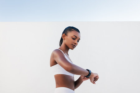 Side view of slim female in white sports bra looking on a smartwatch. Young sportswoman checking heart rate.の写真素材