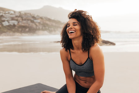 Laughing female with closed eyes sitting on a beach relaxing after an outdoor workoutの写真素材