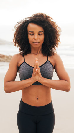 Woman with closed eyes and folded hands standing on a beach and meditatingの写真素材