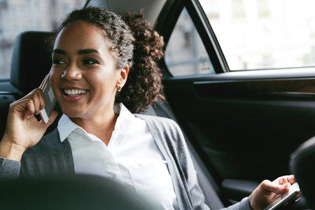 Smiling woman talking on mobile phone, sitting on backseat of taxiの写真素材